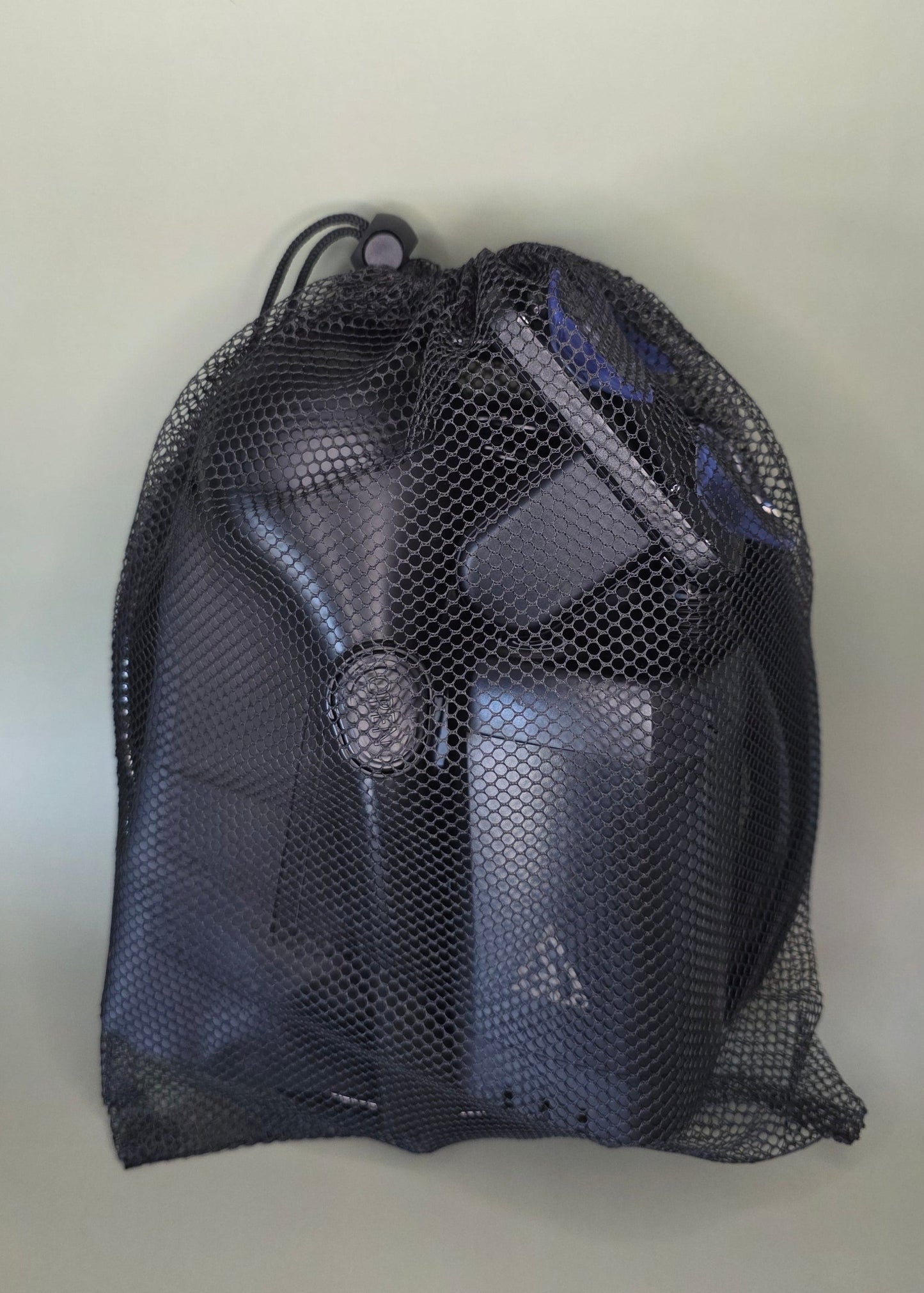 Black mesh bag containing the Avilo portable shower including all accessories with an olive background