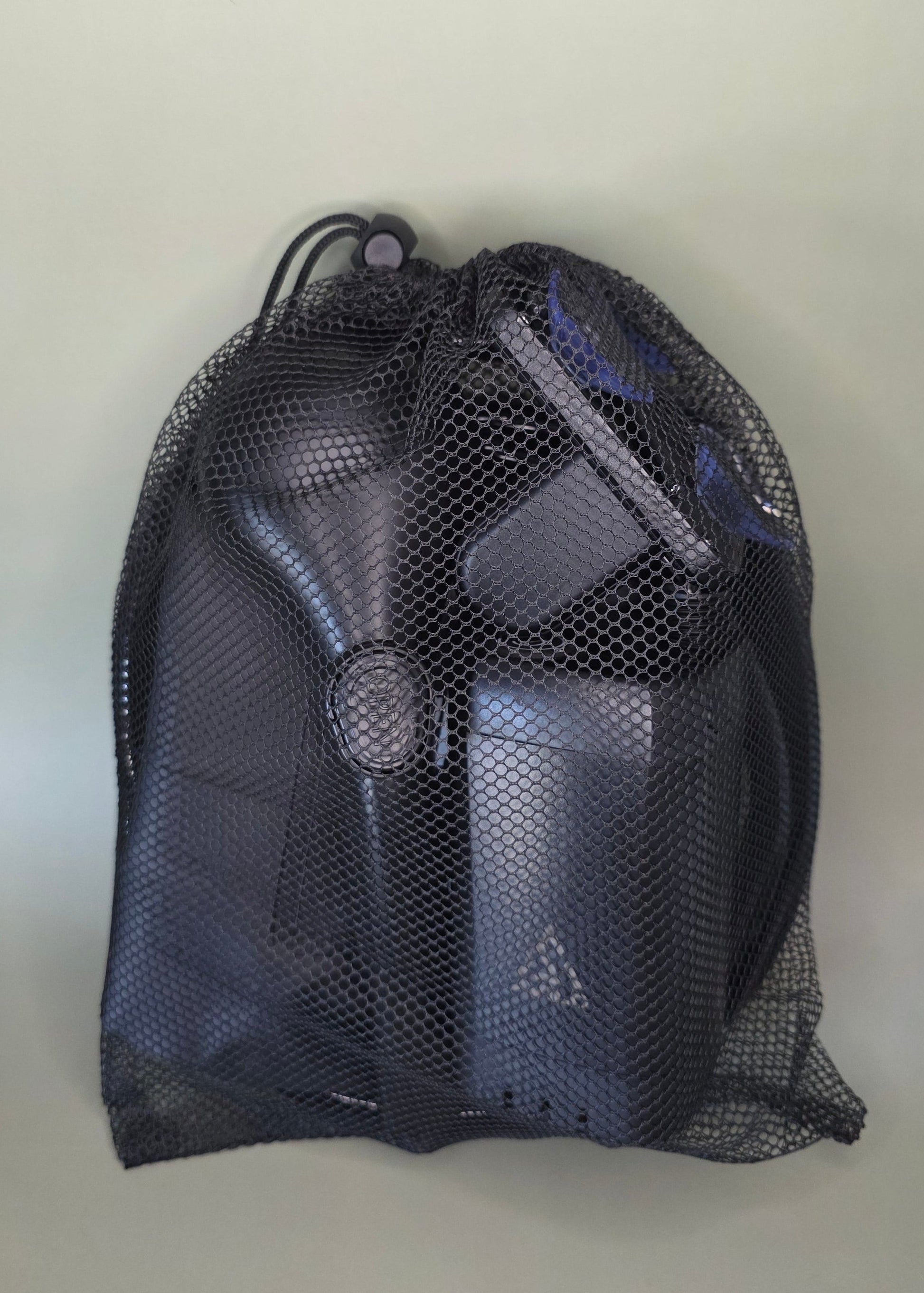 Black mesh bag containing the Avilo portable shower including all accessories with an olive background