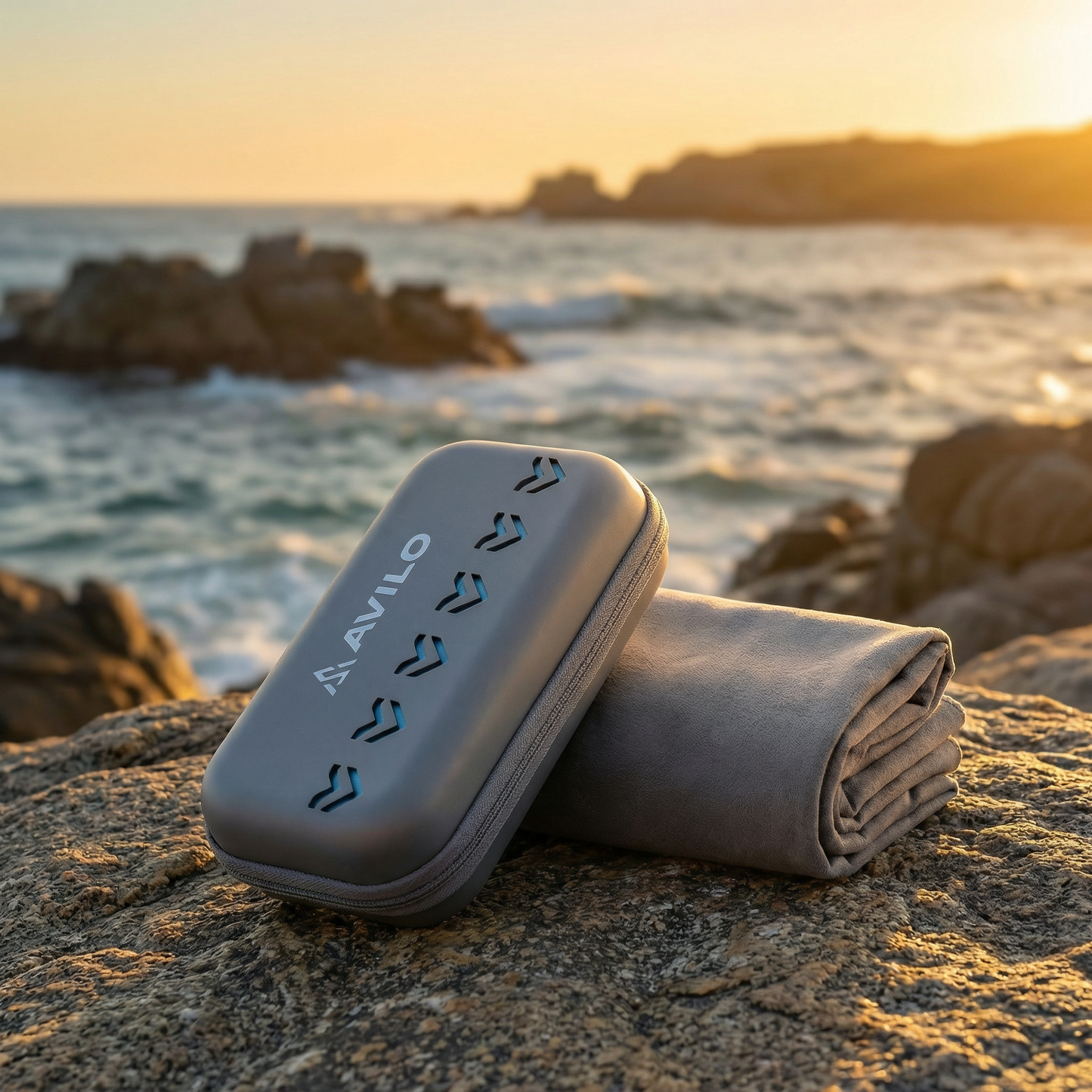 Folded Avilo microfibre towel and carry case on a rocky beach at sunset