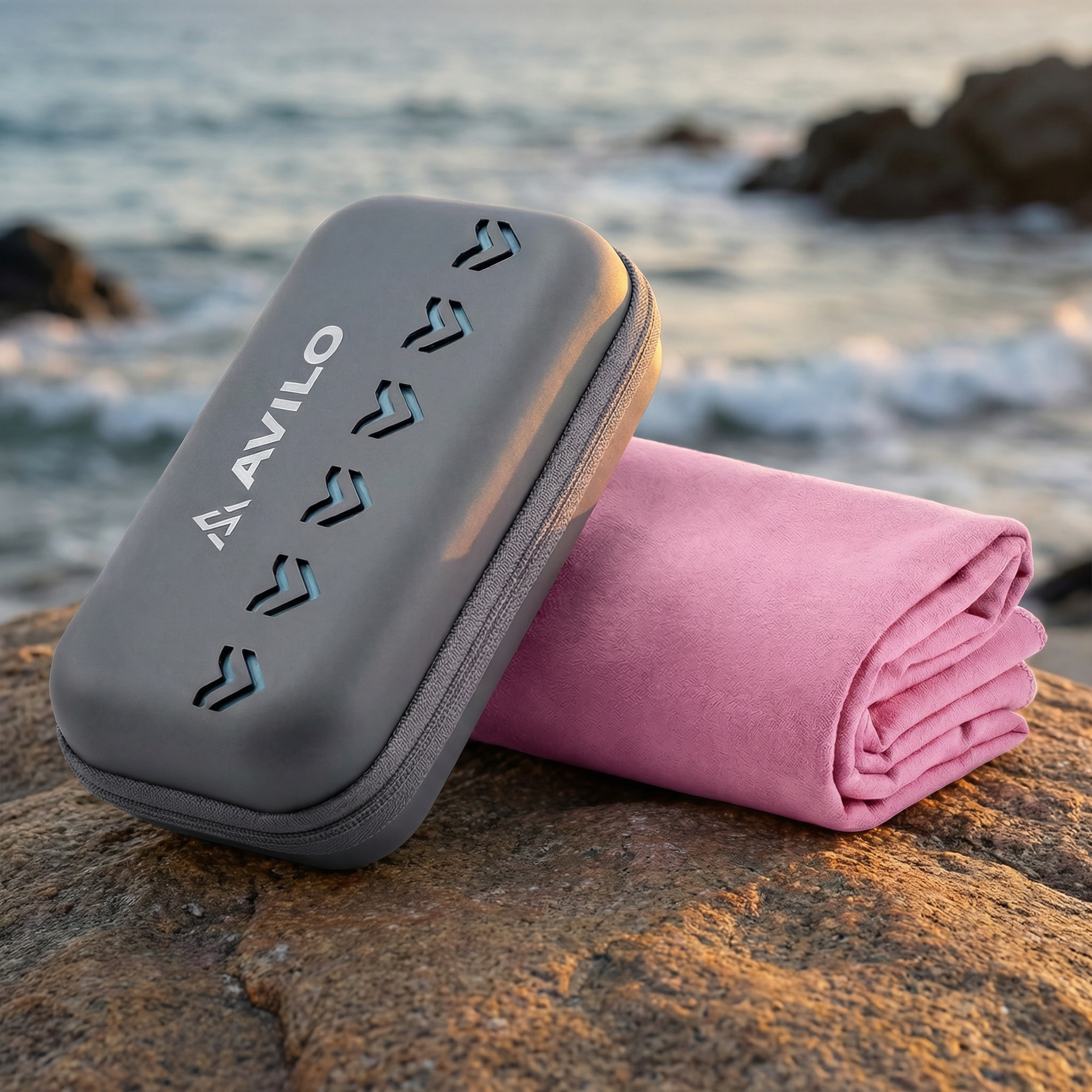 Pink Avilo microfibre towel and grey carry case on a rock by the ocean