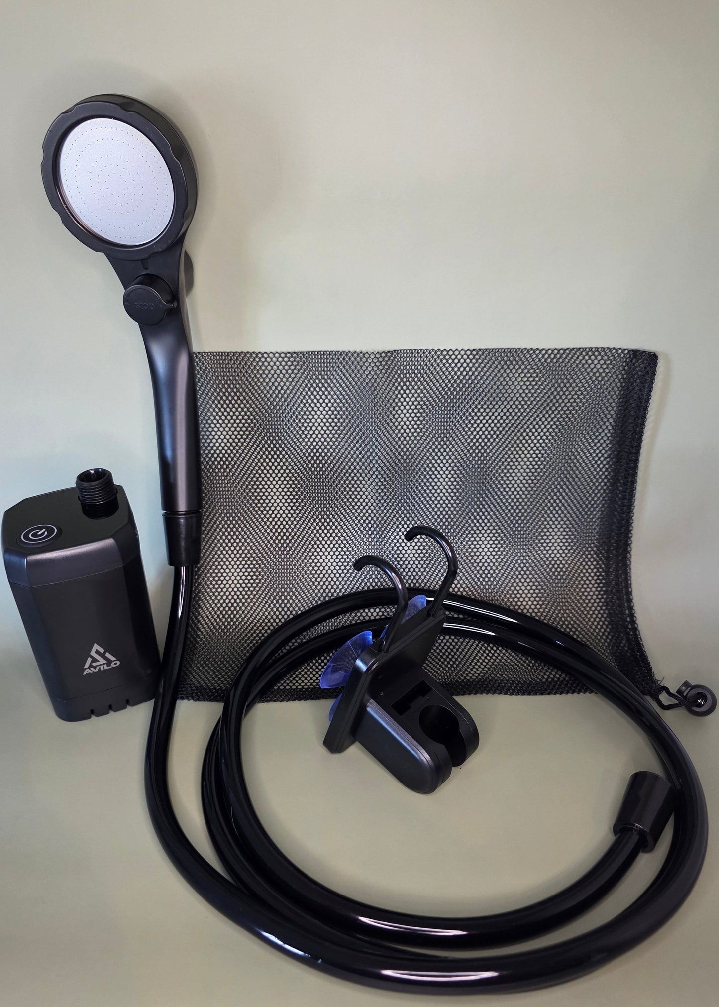 Black portable shower pump with hose, shower head and accessories on an olive background