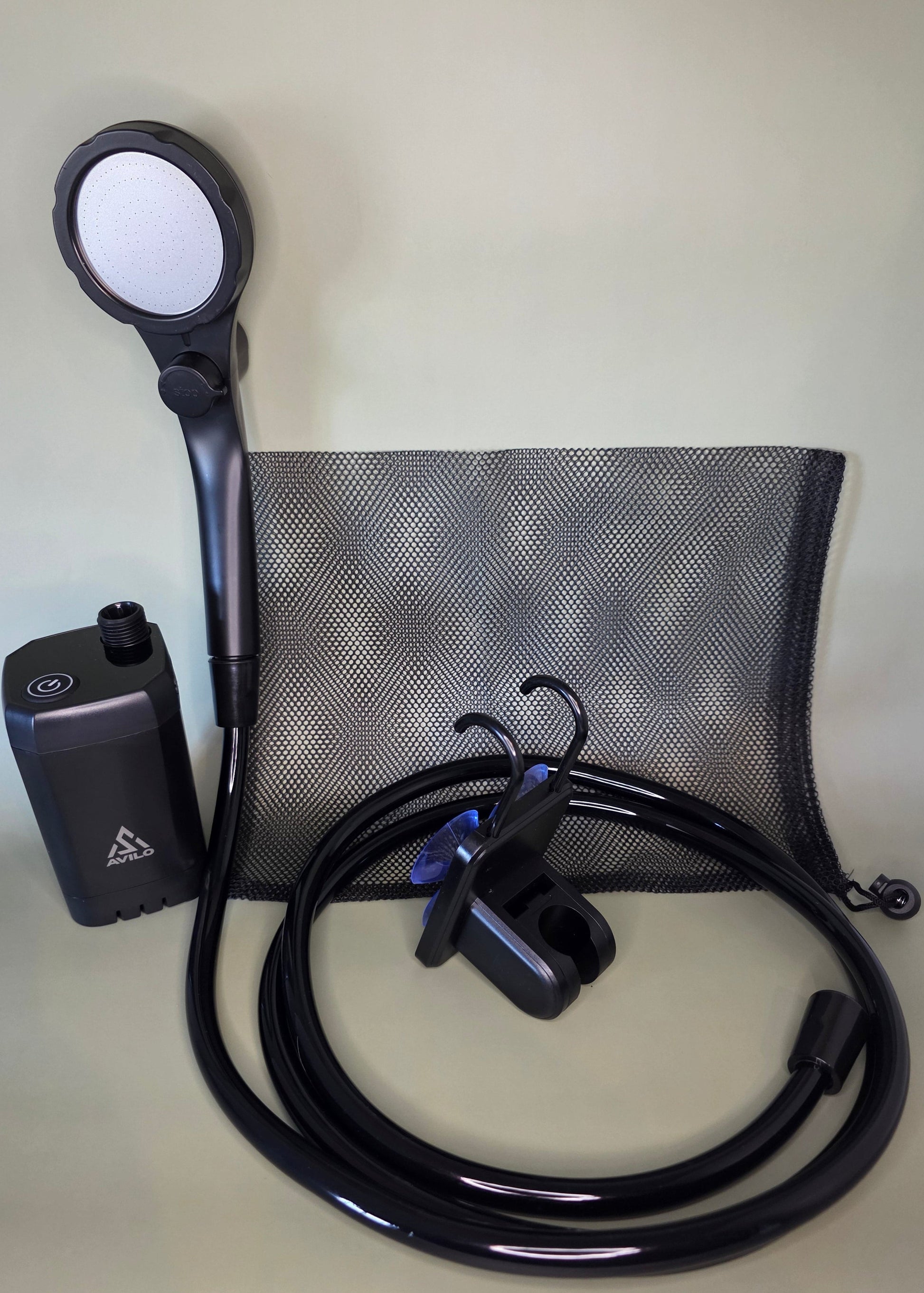 Black portable shower pump with hose, shower head and accessories on an olive background