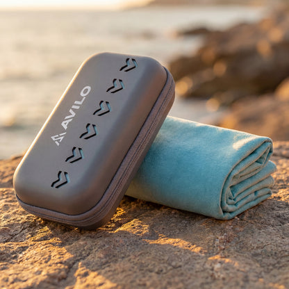 Folded towel and carrying case on a rocky surface with water in the background