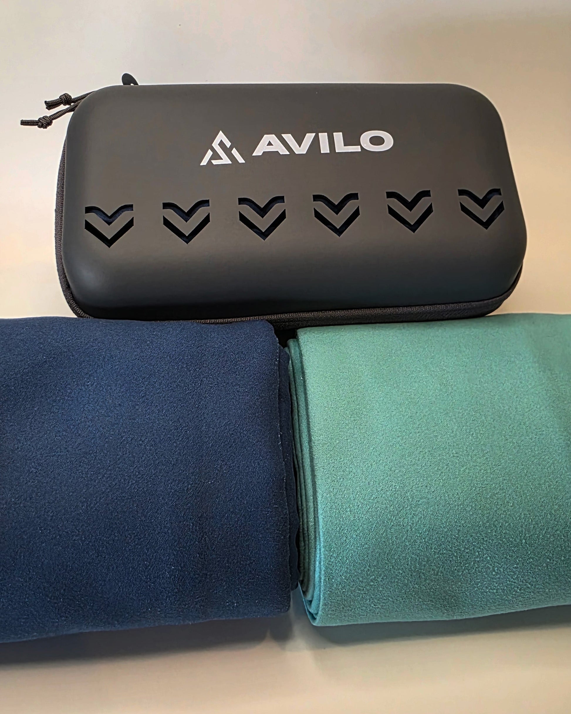 Black pouch with Avilo branding and two folded towels, one blue and one green, on a light background.