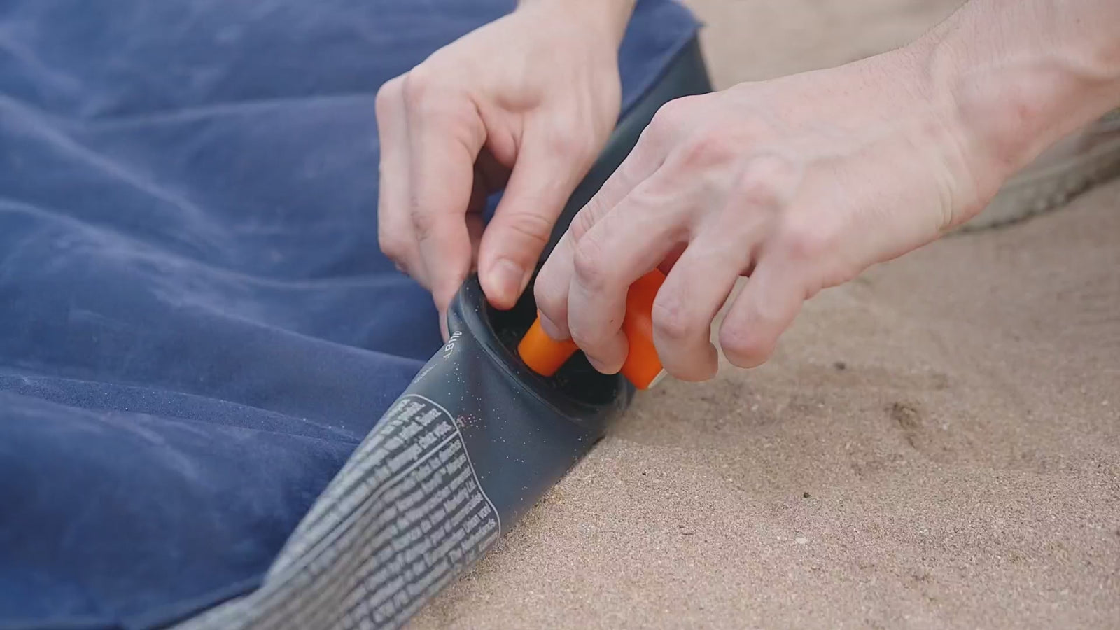 The pump inflating a sleeping mat, a swim ring and a pool float on a beach, sucking a vacuum storage bag flat, then standing in surf foam.